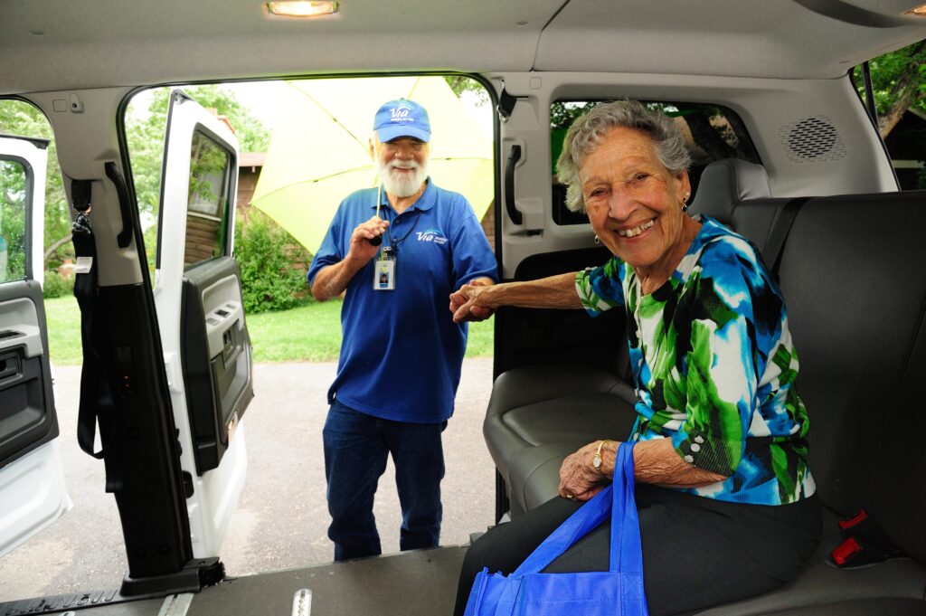 A bus operator holding hands with an older adult sitting in a transit van.