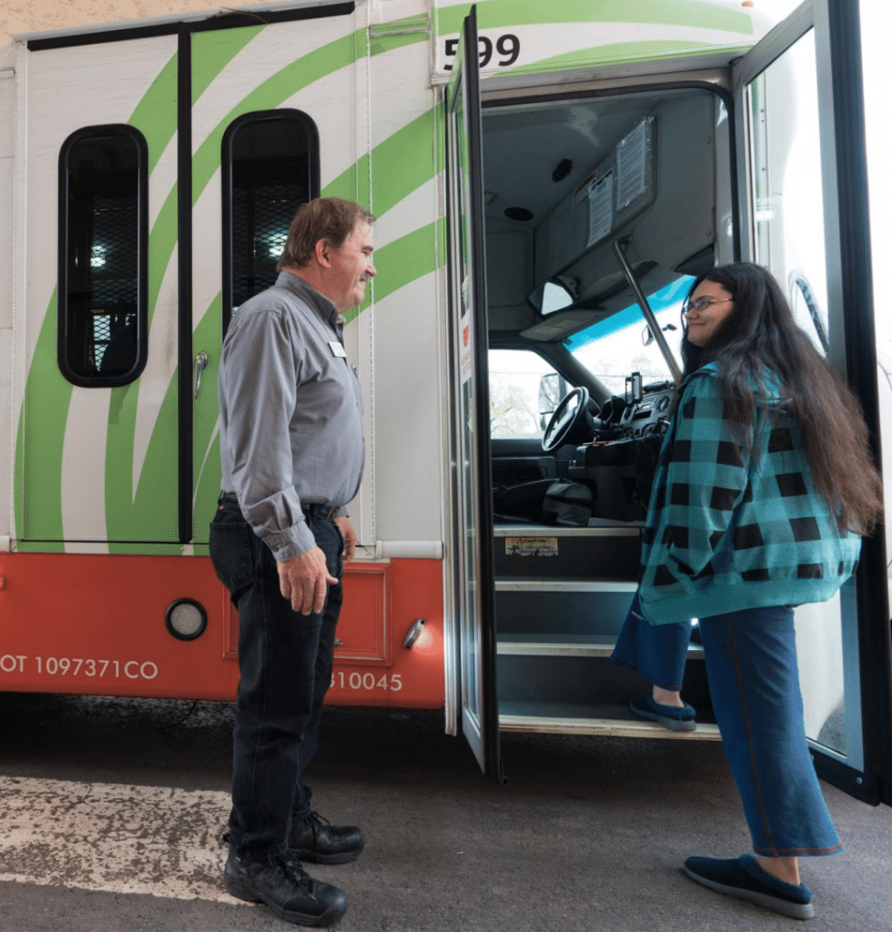 A bus operator greets a woman boarding a small bus.