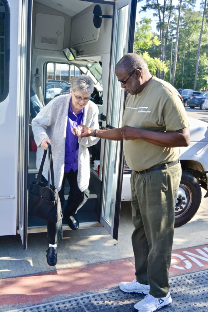 A bus operator assists an older adult exit a small bus.