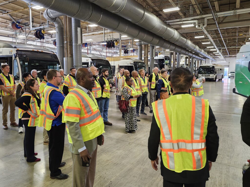 A group of people in yellow vests touring a bus depot